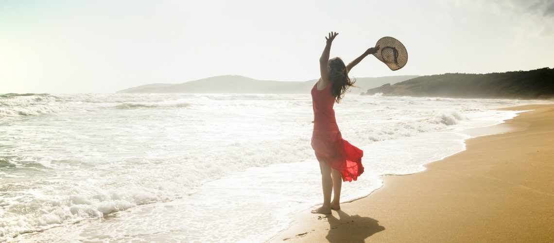 Happy young woman raises her arms towards the sea