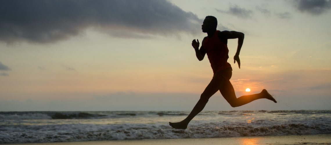 silhouette of young attractive fit athletic and strong black African American man running at sunset beach training hard and sprinting on sea water in professional athlete and runner workout
