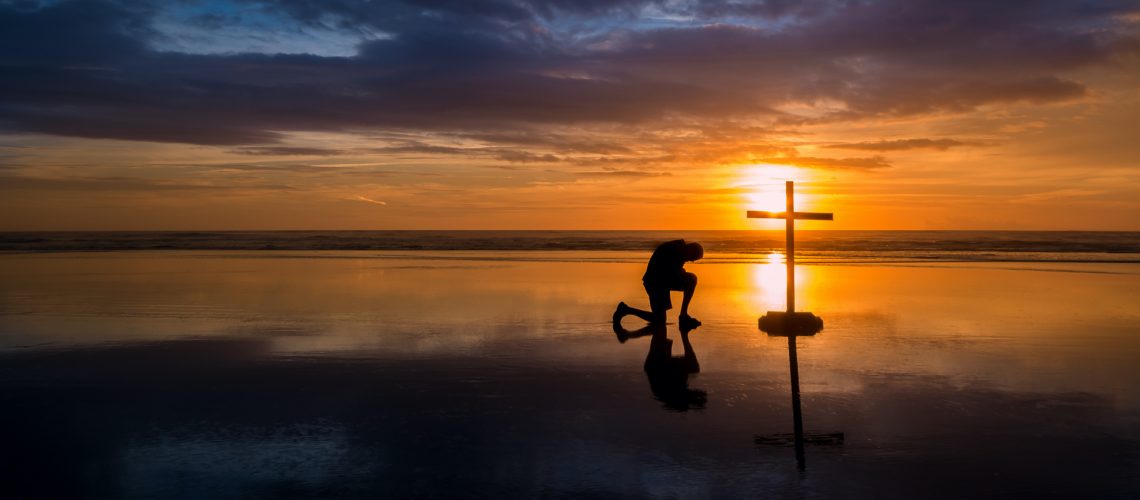 Maravillosa reflexión en una playa al atardecer, con un hombre arrodillado junto a ella.
