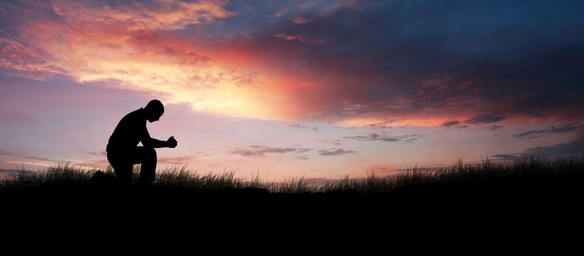 Man kneeling down in a field to pray